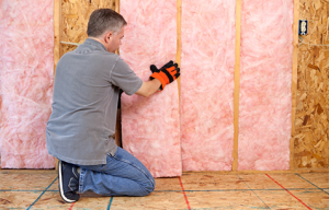 A person installing pink fiberglass batts into a wall 